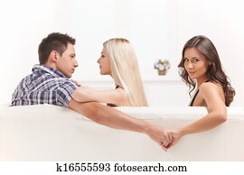 Love triangle. Beautiful young women holding hands with men sitting near his girlfriend
