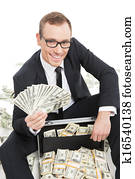 Rich businessman. Happy young businessman in formalwear holding money while sitting near the case full of paper currency