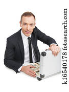 Rich businessman. Happy young businessman in formalwear sitting at the table and holding a suitcase full of money while isolated on white 