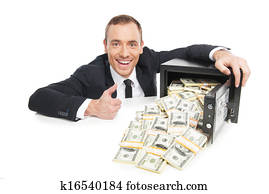 Safe with money. Happy young businessman in formalwear sitting at the table near the safe full of money while isolated on white 