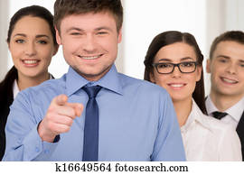 Smiling successful business man pointing with finger on camera. Group of people standing on background Smiling successful business man pointing with finger on camera. Group of people standing on background