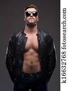 Stylish man. Handsome young man in leather coat and sunglasses standing isolated on grey