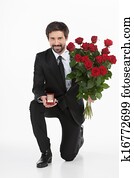 Will you marry me? Young man in full suit standing on one knee and making a proposal while isolated on white background