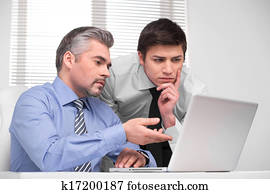 Thoughtful young business man looking at laptop. Adult middle aged durector asking advice 