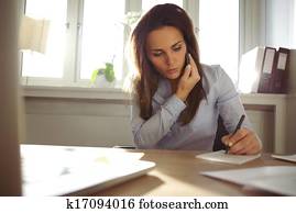 Young female writing notes while talking on phone