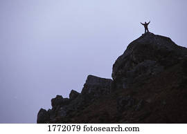 Lone person on mountain peak with arms lifted