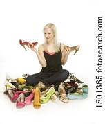 Woman sitting in pile of shoes while holding two high heeled shoes