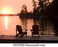 Lake of the Woods, Ontario, Canada, Adirondack chairs on a dock facing the sunset