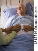 Man in a hospital bed; Man's hand being held by a woman