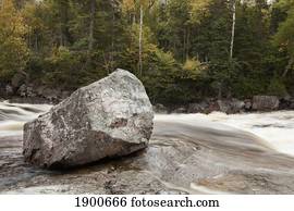 a river rushing past a boulder in autumn; ontario, canada