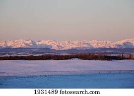 sunrise over canadian rockies and snowy field; cochrane, alberta, canada