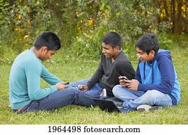 three brothers using their cell phones for texting in a park; edmonton alberta canada