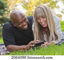 Interracial Couple Looking At Text Messages In The Park; Edmonton Alberta Canada