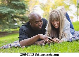 Interracial Couple Looking At Text Messages In The Park; Edmonton Alberta Canada