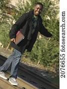 Teenage boy holding a school book and walking on railroad tracks; portland oregon united states of america