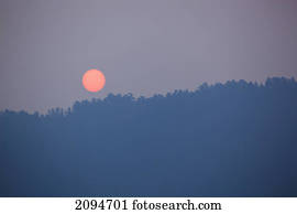 An orange sun rises into a smokey summer sky; desolation sound, british columbia, canada