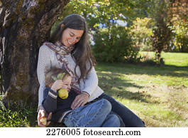A mother and her young son sit under a heritage apple tree on a farm; british columbia canada
