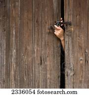 A hand reaching out a wooden door to unlock a padlock