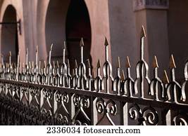 A metal railing with sharp pointed edges on top and a building with arched doorways