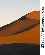 A person stands on a top ridge of a sand slope