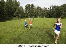 Kids running across a grass field in a park with the parents in the background; Stony Plain, Alberta, Canada
