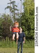 A boy swinging on a swing set with his father in the background; Stony Plain, Alberta, Canada