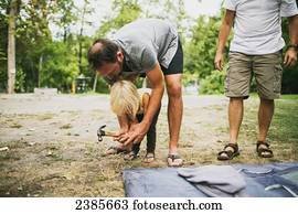 A father and young daughter work together to hammer in tent pegs at a campsite; Peachland, British Columbia, Canada