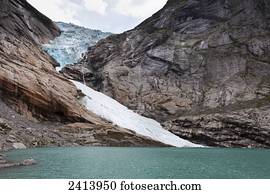 A glacier on a rugged mountain at the water's edge; Olden, Norway