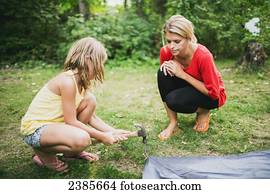 A mother watches her daughter hammer in a tent peg; Peachland, British Columbia, Canada
