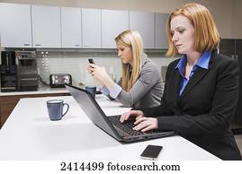 Co-workers on a break, texting and working on a computer; Edmonton, Alberta, Canada