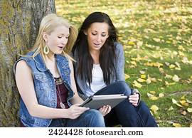 Two friends looking at a tablet in a park in autumn; Edmonton, Alberta, Canada
