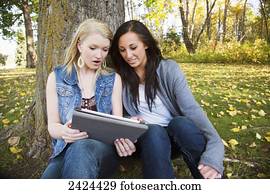 Two friends looking at a tablet in a park in autumn; Edmonton, Alberta, Canada
