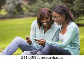 Two sisters using smart phones in the park; Edmonton, Alberta, Canada
