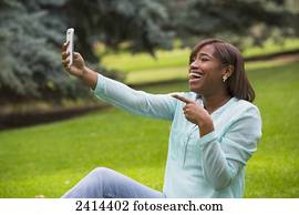Young woman taking a self-portrait with her smart phone in the park; Edmonton, Alberta, Canada