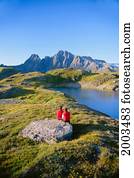 Alaska, Juneau, View Of Couple Sitting Beside Lake In Snow Capped Mountains, Blue Sky
