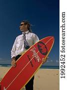 Man Standing On Beach In Business Suit Holding A Surfboard.