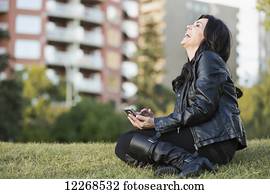 Mature woman laughing at message on her smart phone in an outdoor urban park in autumn; Edmonton, Alberta, Canada
