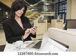 Professional businesswoman text messages while reviewing construction plans for office interior; Edmonton, Alberta, Canada