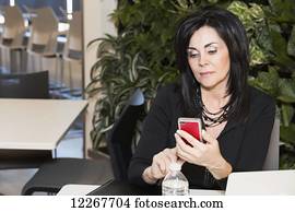 Professional businesswoman texting while taking a break in a cafeteria; Edmonton, Alberta, Canada Professional businesswoman texting while taking a break in a cafeteria; Edmonton, Alberta, Canada