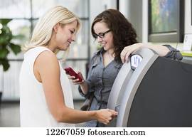Two girlfriends getting money from an ATM machine at the mall; St. Albert, Alberta, Canada