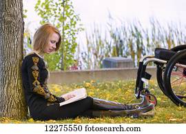 jonge, gehandicapte vrouw, zittende, naast, haar, wheelchair, het lezen van een boek, in, een, stad park, in, autumn;, edmonton, alberta, canada