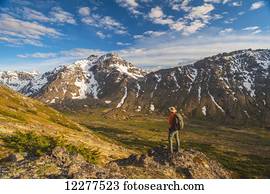 Hiker on rock outcrop overlooks Powerline Pass valley and trail, Chugach State Park, Southcentral Alaska