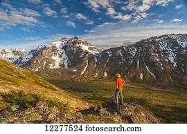 Hiker on rock outcrop overlooks Powerline Pass valley and trail, Chugach State Park, Southcentral Alaska