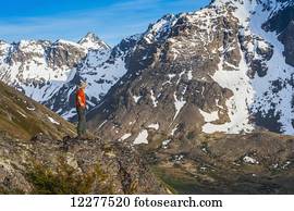 Hiker on rock outcrop overlooks Powerline Pass valley and trail, Chugach State Park, Southcentral Alaska