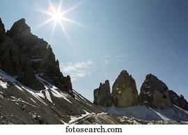 Rugged mountain spires with sunburst and blue sky; Sesto, Bolzano, Italy
