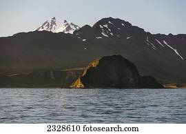 Frosty Volcano Peaking Out From Behind A Ridgeline With Aagat Island In The Foreground Near Cold Bay On The Alaska Peninsula; Southwest Alaska, United States Of America