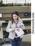 Business woman on an escalator talking on her cell phone, checking the time and holding a tablet; Edmonton, Alberta, Canada
