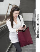 Business woman texting on her smart phone on an escalator after taking a shopping break during her work day; Edmonton, Alberta, Canada Business woman texting on her smart phone on an escalator after taking a shopping break during her work day; Edmonton, Alberta, Canada