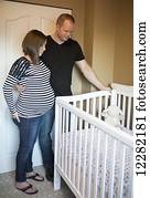 Couple expecting a baby and standing by the crib; Langley, British Columbia, Canada