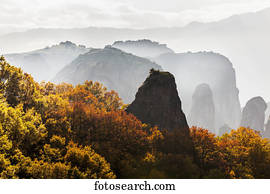 Low cloud around the rugged cliffs with foliage in autumn colours; Meteora, Greece